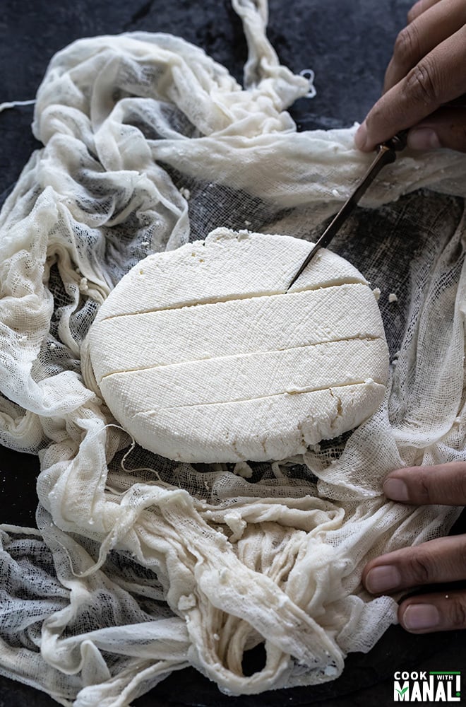 knife cutting a block of freshly made paneer placed in a muslin cloth