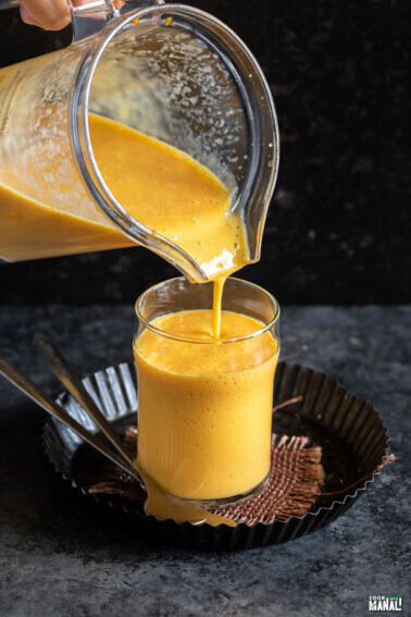 mango milkshake being poured into a glass from a blender