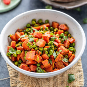 carrots and green peas stir fry in a white bowl and few rotis placed in the background