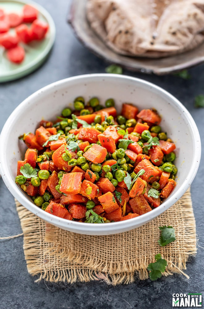 carrots and green peas stir fry in a white bowl and few rotis placed in the background