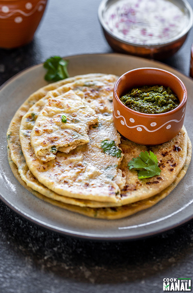 paneer paratha in a round plate with a bowl of cilantro chutney