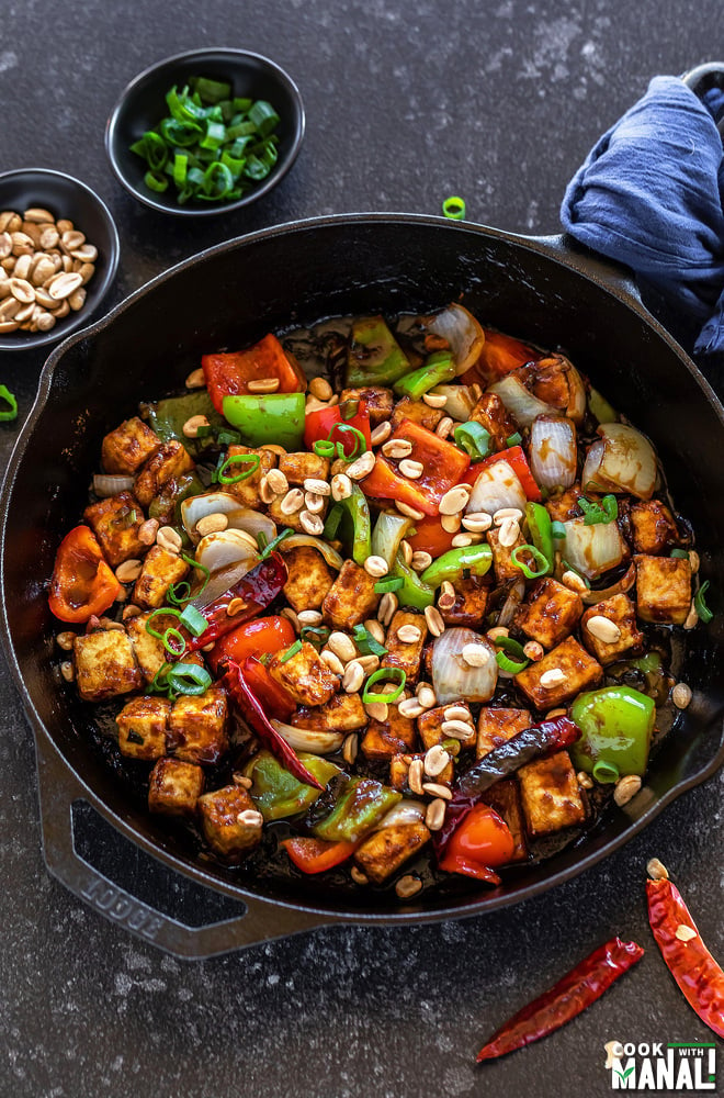 kung pao tofu served in a cast iron skillet with bowls of peanuts and chopped green onions placed in the background