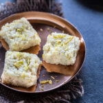 3 pieces of kalakand served on a small round copper plate with a tealight in the background
