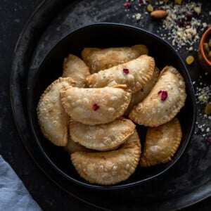 a bowl full of gujiya with a small bowl of nuts on the side