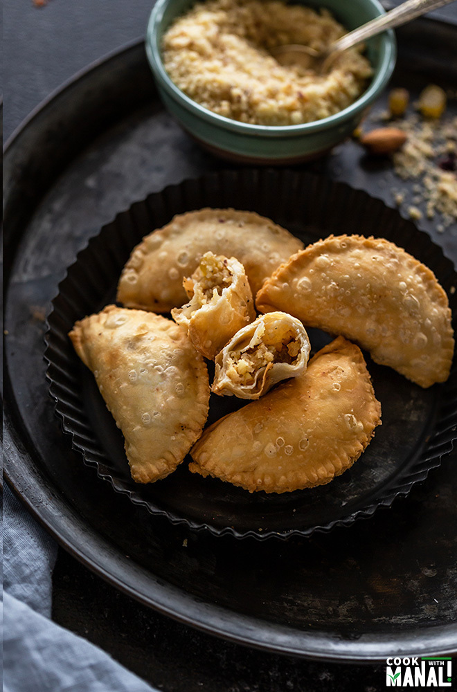 5 gujiya is a black plate with one gujiya being cut into two parts to show the filling