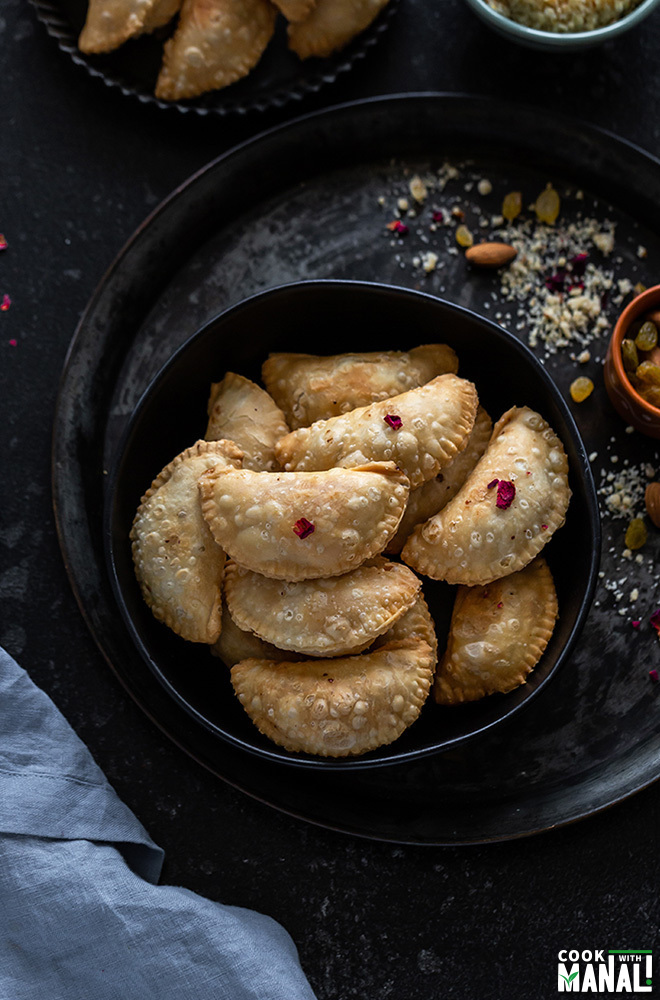 a bowl full of gujiya with a small bowl of nuts on the side