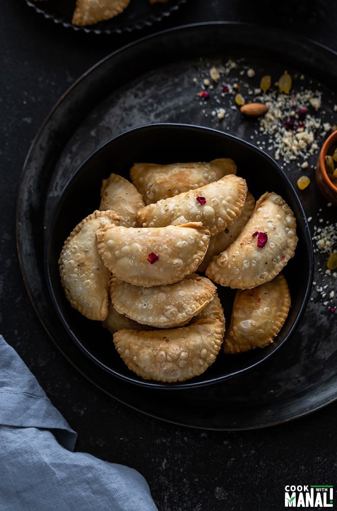 a bowl full of gujiya with a small bowl of nuts on the side