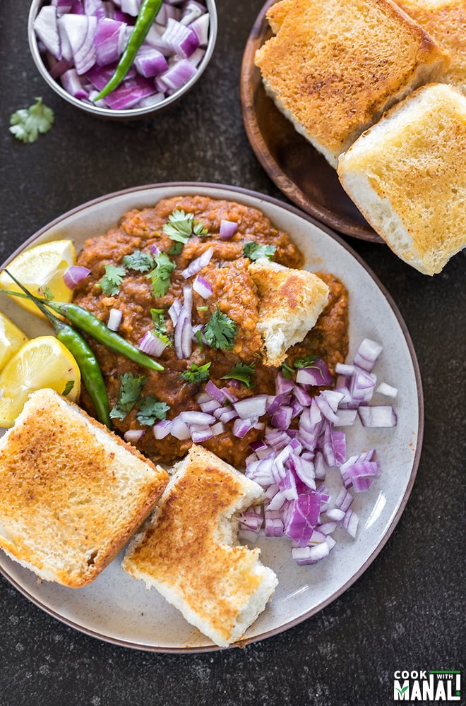 pav bhaji in a round plate served with a side of green chili, lemon slices and chopped onions