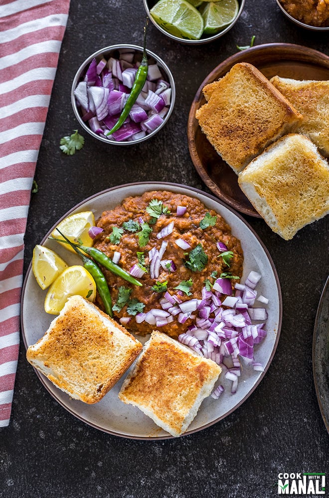 pav bhaji in a round plate served with a side of green chili, lemon slices and chopped onions