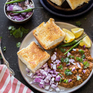 pav bhaji in a round plate served with a side of green chili, lemon slices and chopped onions
