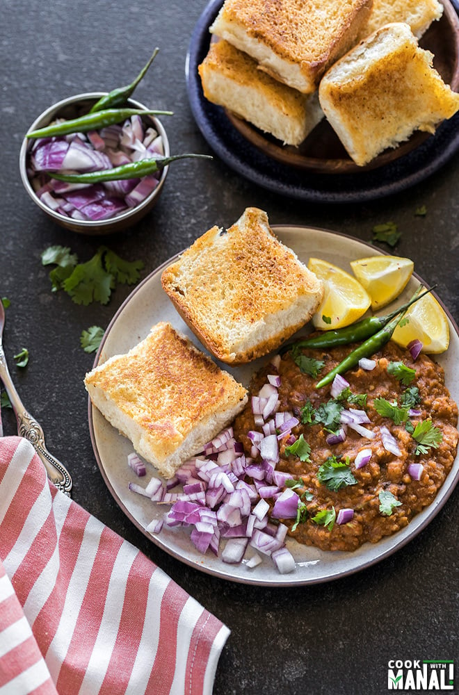 pav bhaji in a round plate served with a side of green chili, lemon slices and chopped onions