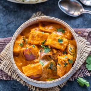 paneer curry served in a white bowl garnished with cilantro with naan in the background