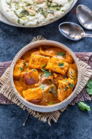paneer curry served in a white bowl garnished with cilantro with naan in the background