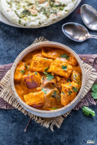 paneer curry served in a white bowl garnished with cilantro with naan in the background