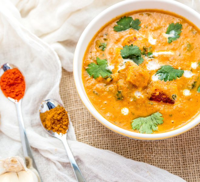 bowl of paneer tikka masala garnished with cilantro and spoons of spices placed on the side