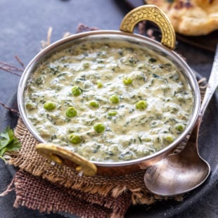 methi matar malai served in a copper kadai with a naan placed in the back