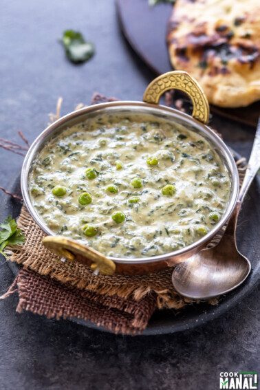 methi matar malai served in a copper kadai with a naan placed in the back