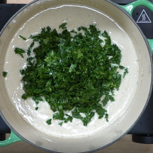 fresh fenugreek leaves being added to a white curry