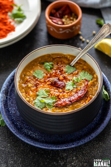 dal tadka in a black bowl garnished with cilantro with a spoon and some spices in the background