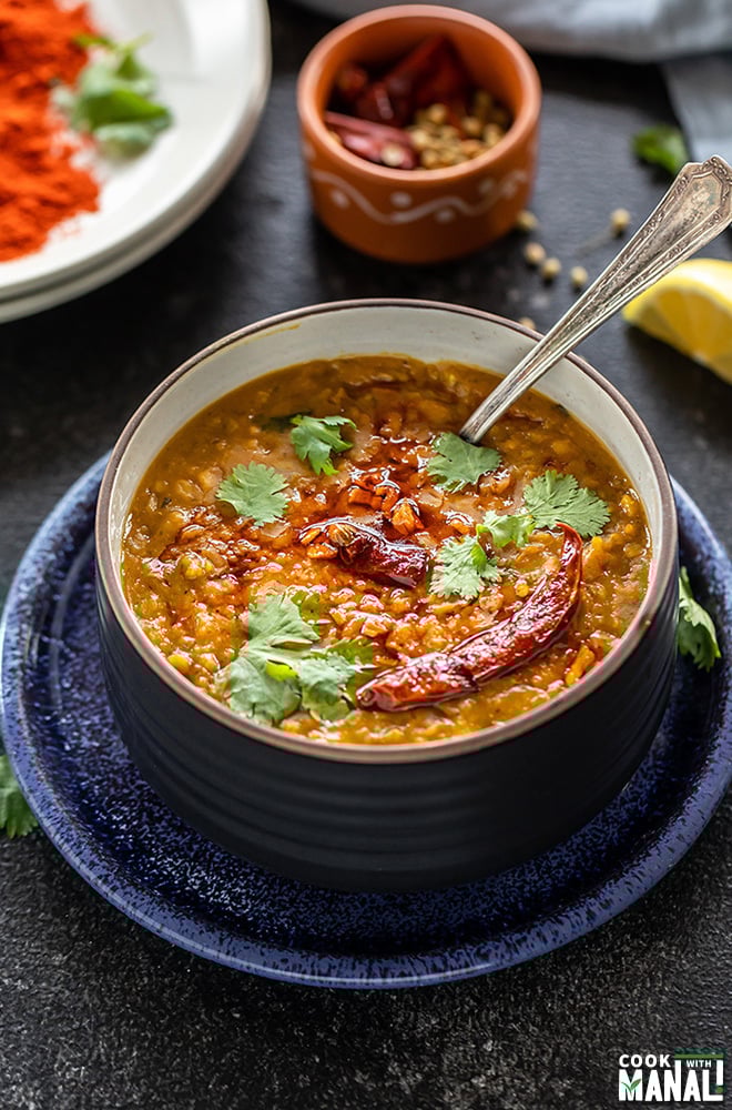 dal tadka w czarnej misce przyozdobiona kolendrą z łyżką i kilkoma przyprawami w tle