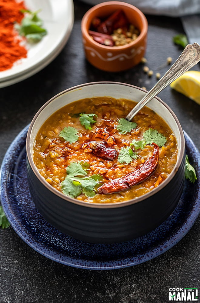 dal tadka en un bol negro adornado con cilantro con una cuchara y algunas especias al fondo