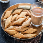 namak para served in a bronze plate with glass of chai on the side