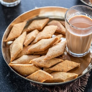 namak para served in a bronze plate with glass of chai on the side