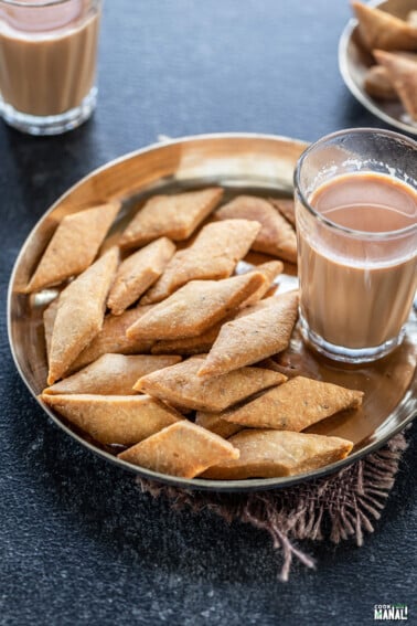 namak para served in a bronze plate with glass of chai on the side