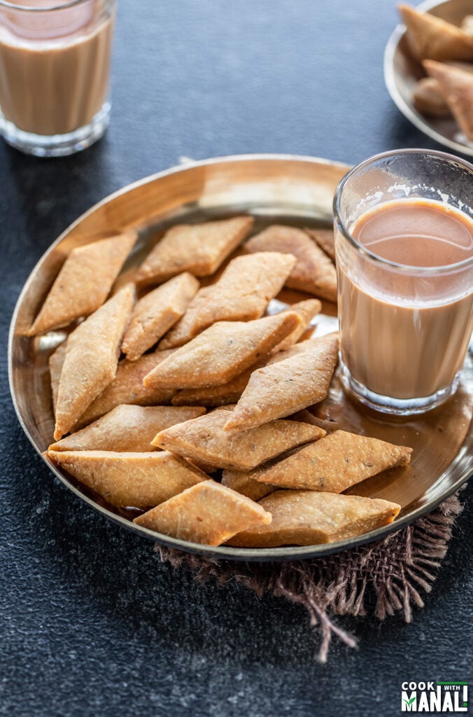 namak para served in a copper plate with glass of chai on the side