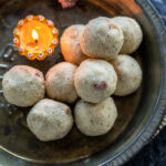 rava ladoos stacked on a plate with a diya placed on the side
