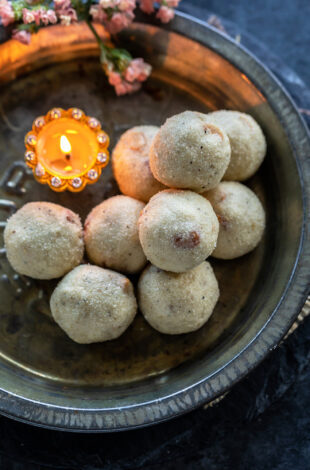 rava ladoos stacked on a plate with a diya placed on the side