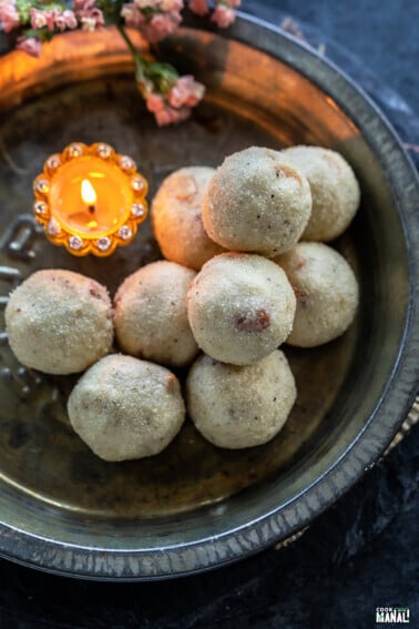 rava ladoos stacked on a plate with a diya placed on the side