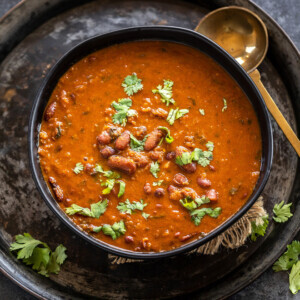 Kidney beans curry served in a black bowl garnished with cilantro with a golden color ladle placed on the side of the bowl