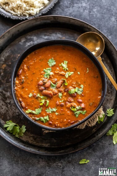 Kidney beans curry served in a black bowl garnished with cilantro with a golden color ladle placed on the side of the bowl