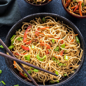 hakka noodles in a black bowl with a pair of chopsticks