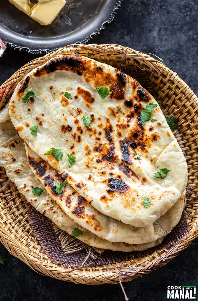 homemade naan stacked and placed on a round bamboo bowl