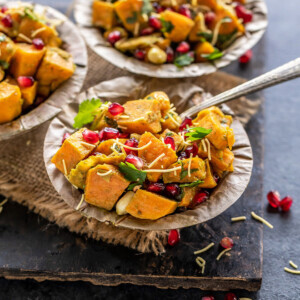 three bowls of sweet potato chaat topped with pomegranate, cilantro and sev