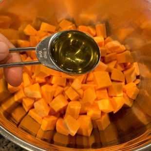 tablespoon of oil being added to a bowl of diced sweet potatoes