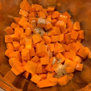 salt and spices being added to a bowl of sweet potatoes