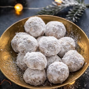 cookies coated in powdered sugar placed on a golden plate with lights in the background