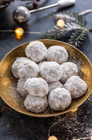 cookies coated in powdered sugar placed on a golden plate with lights in the background