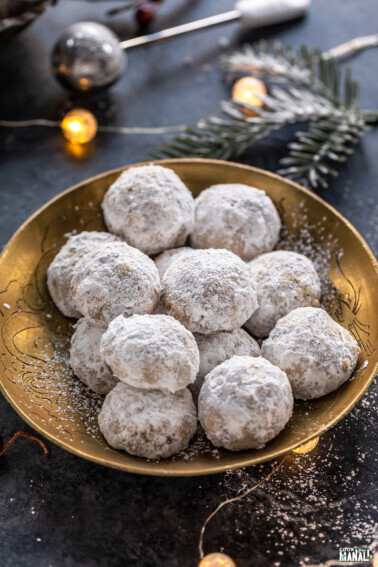 cookies coated in powdered sugar placed on a golden plate with lights in the background