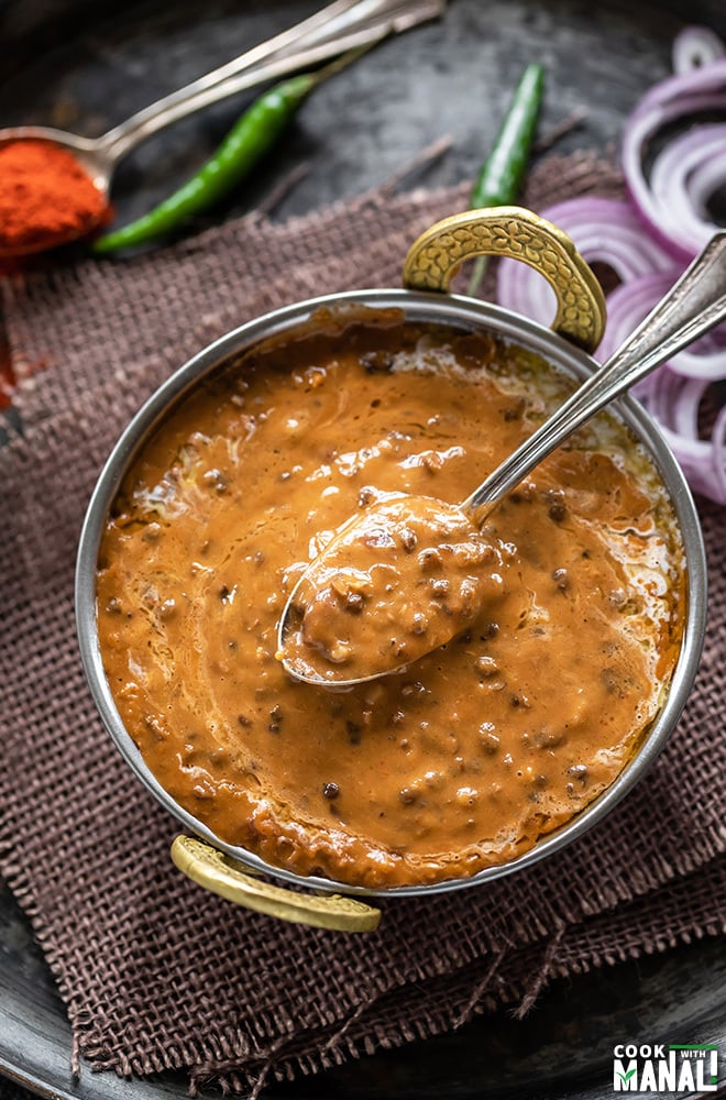 dal makhani served it a kadai with a spoon with some onion slices in the background