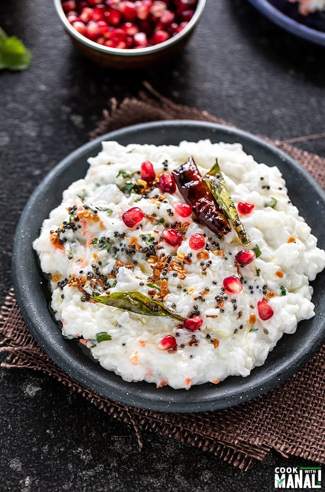 curd rice in a black plate garnished with pomegranate and a bowl of pomegranate arils in the background