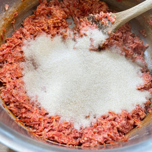 sugar being added to a pot of grated carrots