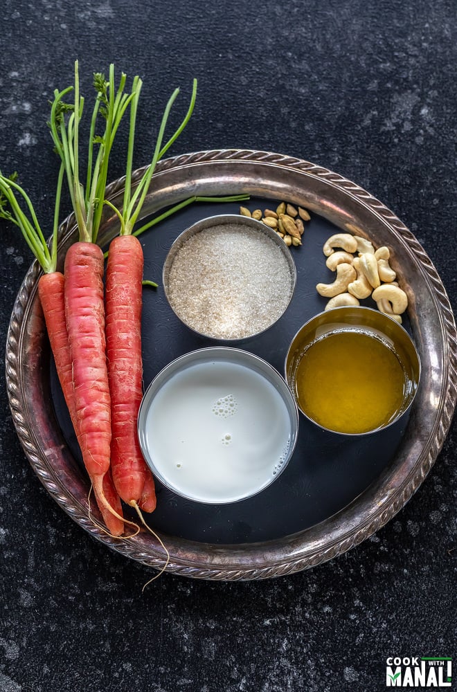 red carrots, sugar, milk, ghee, cashews and cardamom placed on a plate