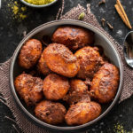 kashmiri dum aloo in a bowl with bowl of spices and whole spices scattered around