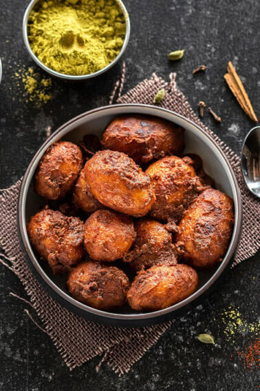 kashmiri dum aloo in a bowl with bowl of spices and whole spices scattered around