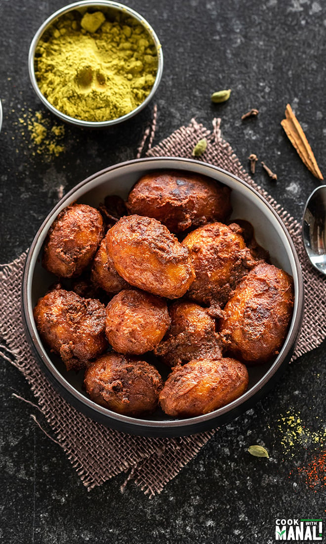 kashmiri dum aloo in a bowl with bowl of spices and whole spices scattered around