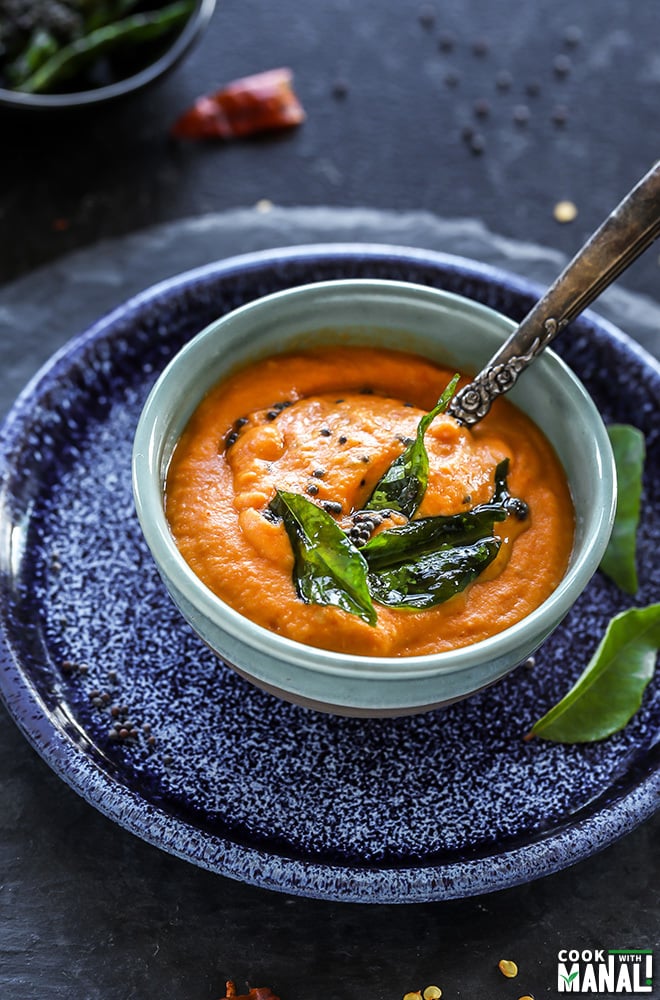 bowl of tomato chutney with a spoon placed on a blue round plate